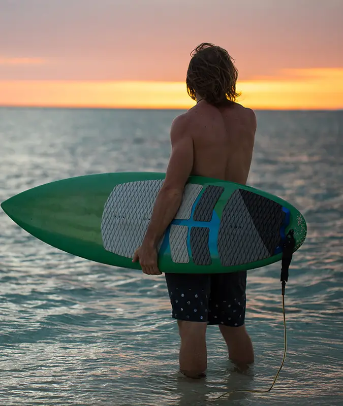 Hombre de espaldas mirando al mar con una tabla de surf