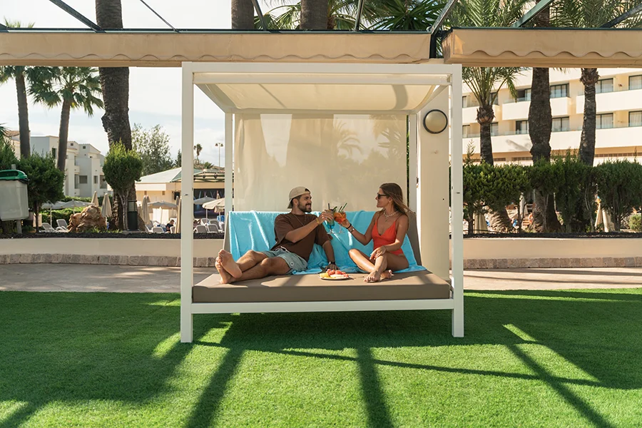 Pareja brindado con un cóctel sobre una cama balinesa Welikehotel Marfil Playa 